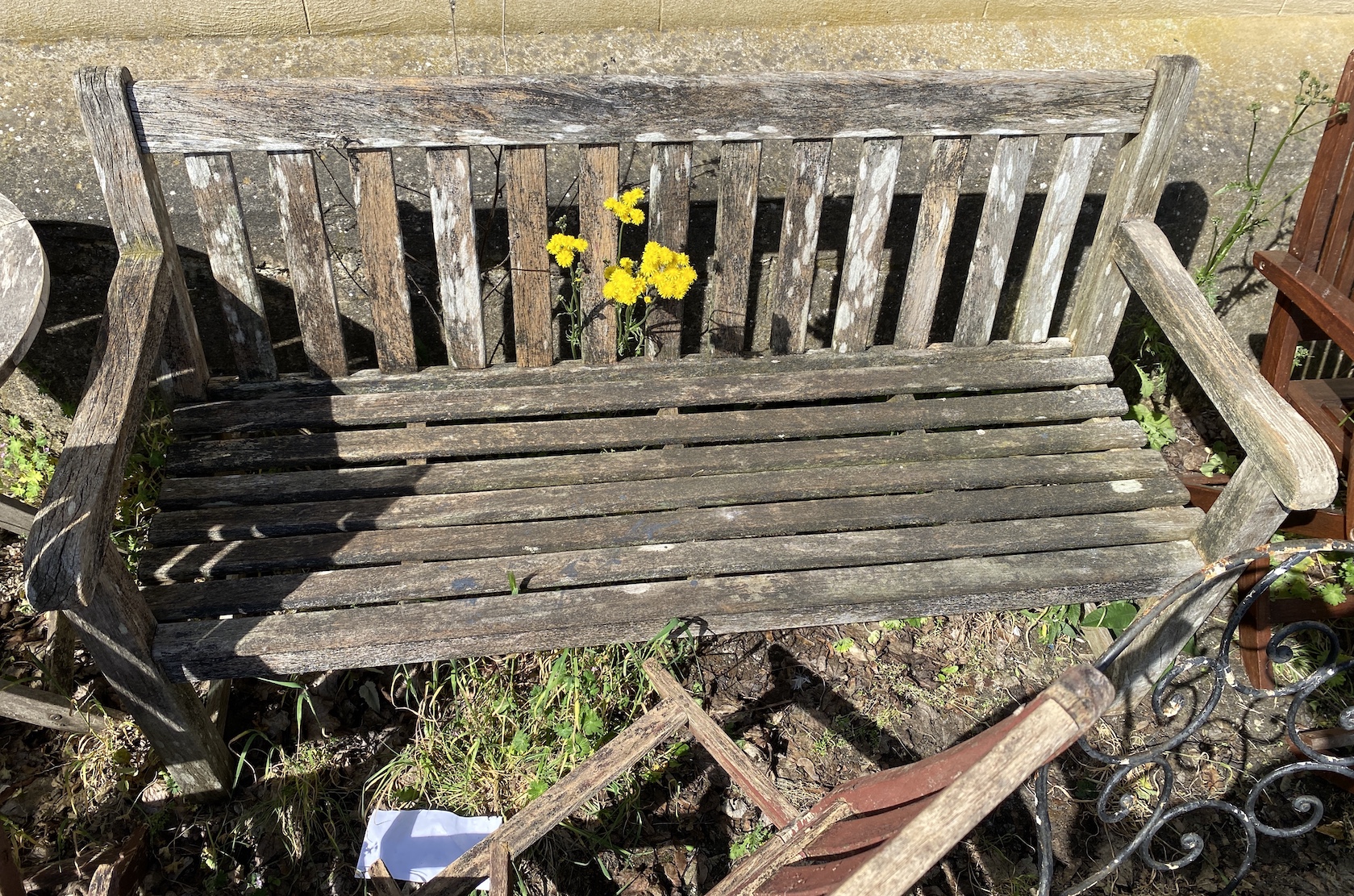 A weathered teak garden bench, width 148cm, height 88cm, a circular folding table and three folding chairs